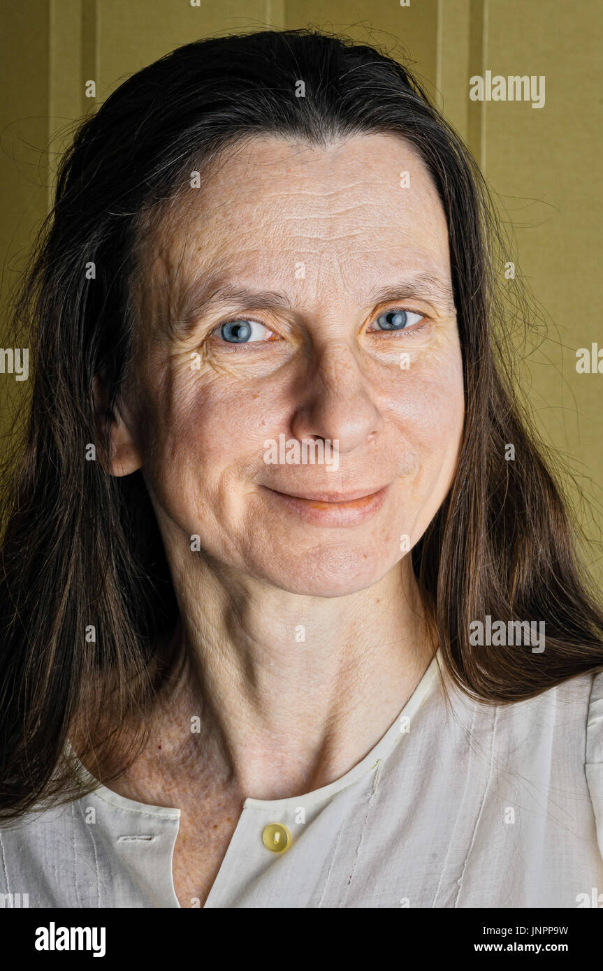 A happy adult woman with long hair is  smiling with a warm and positive expression Stock Photo