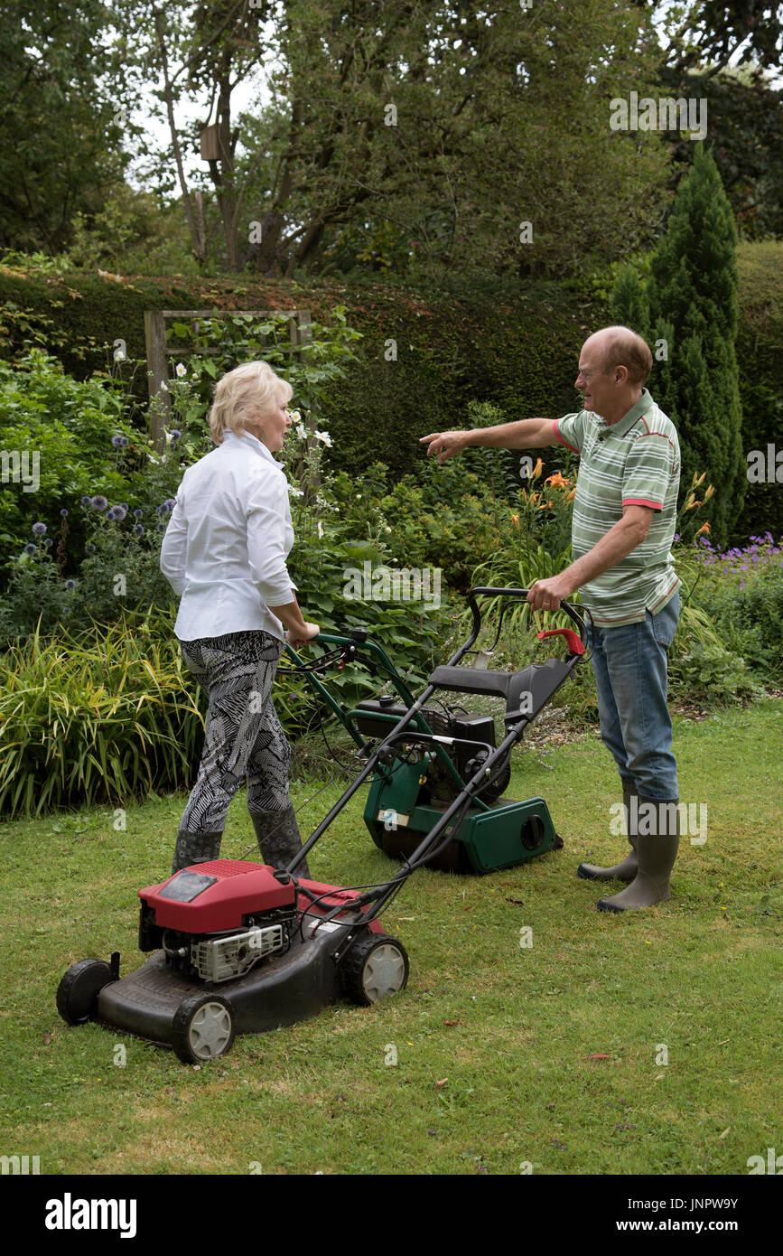 Man and woman with lawn mowers working in a country garden. Man pointing. Stock Photo