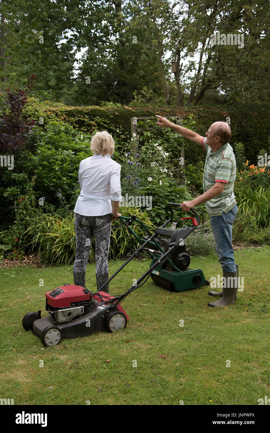 Man and woman with lawn mowers working in a country garden. Man pointing. Stock Photo