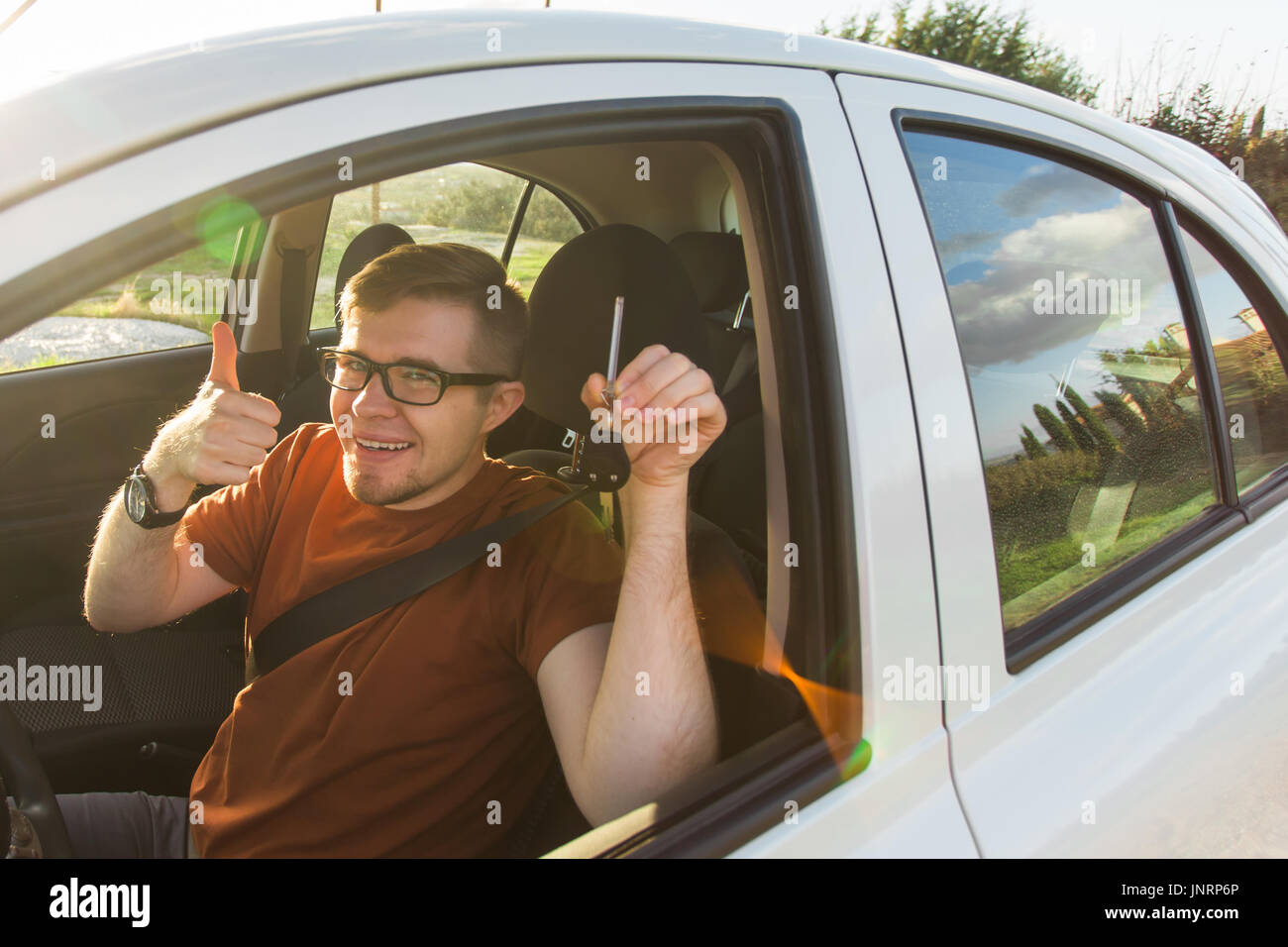 Young driver showing car keys and thumbs up happy. Man holding car key