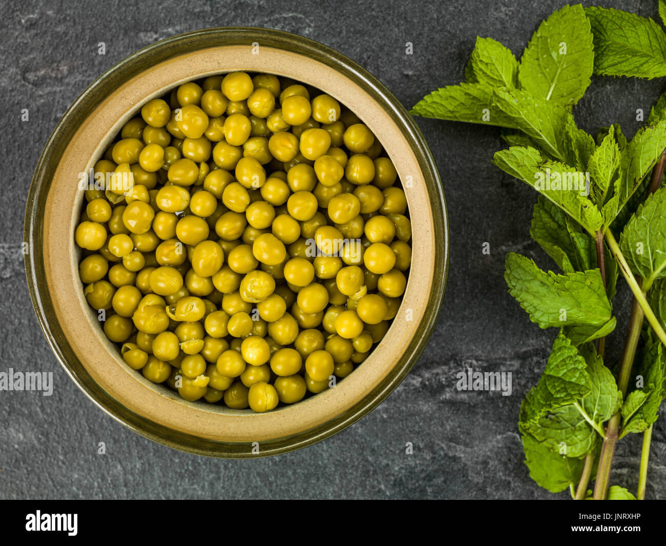 Bowl of Fresh Summer Garden Peas With Fresh Mint Against a Black Slate Background Stock Photo