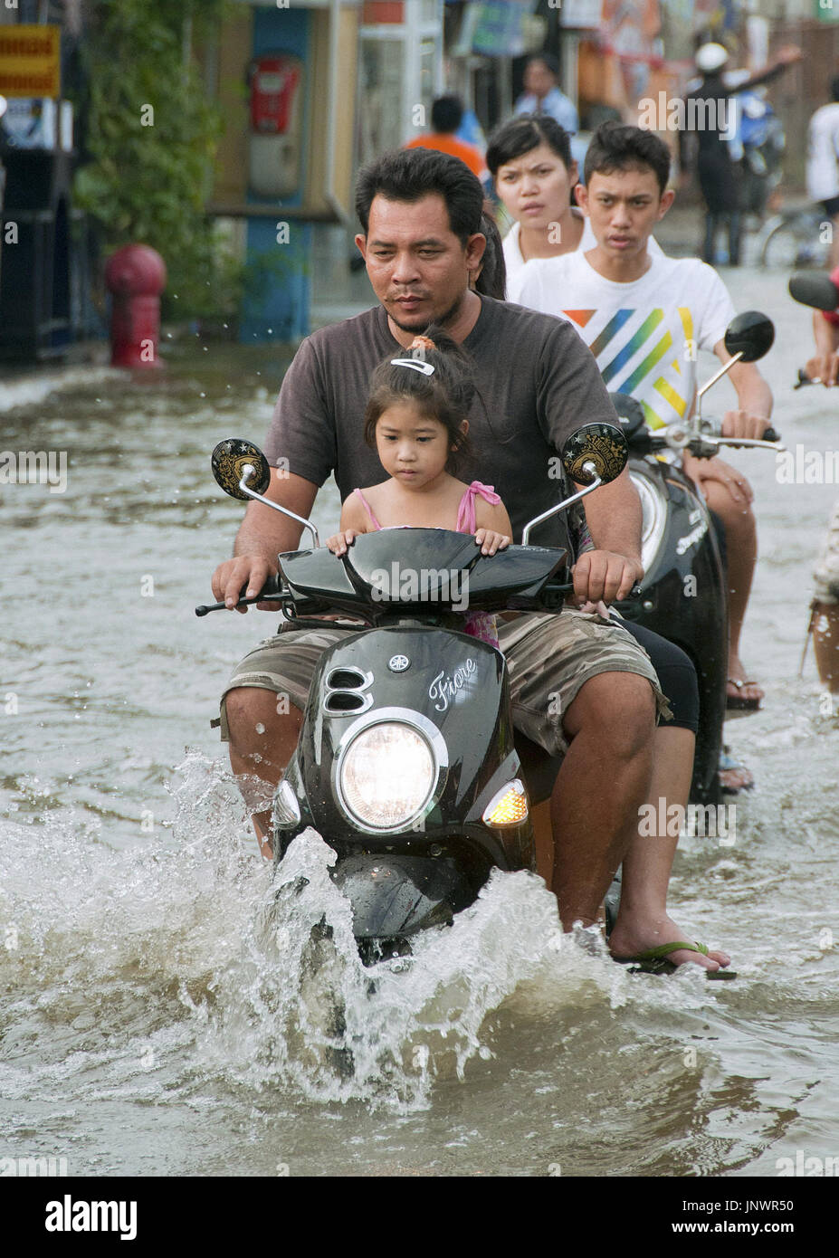 BANGKOK, Thailand People ride motor scooters on a flooded street in a