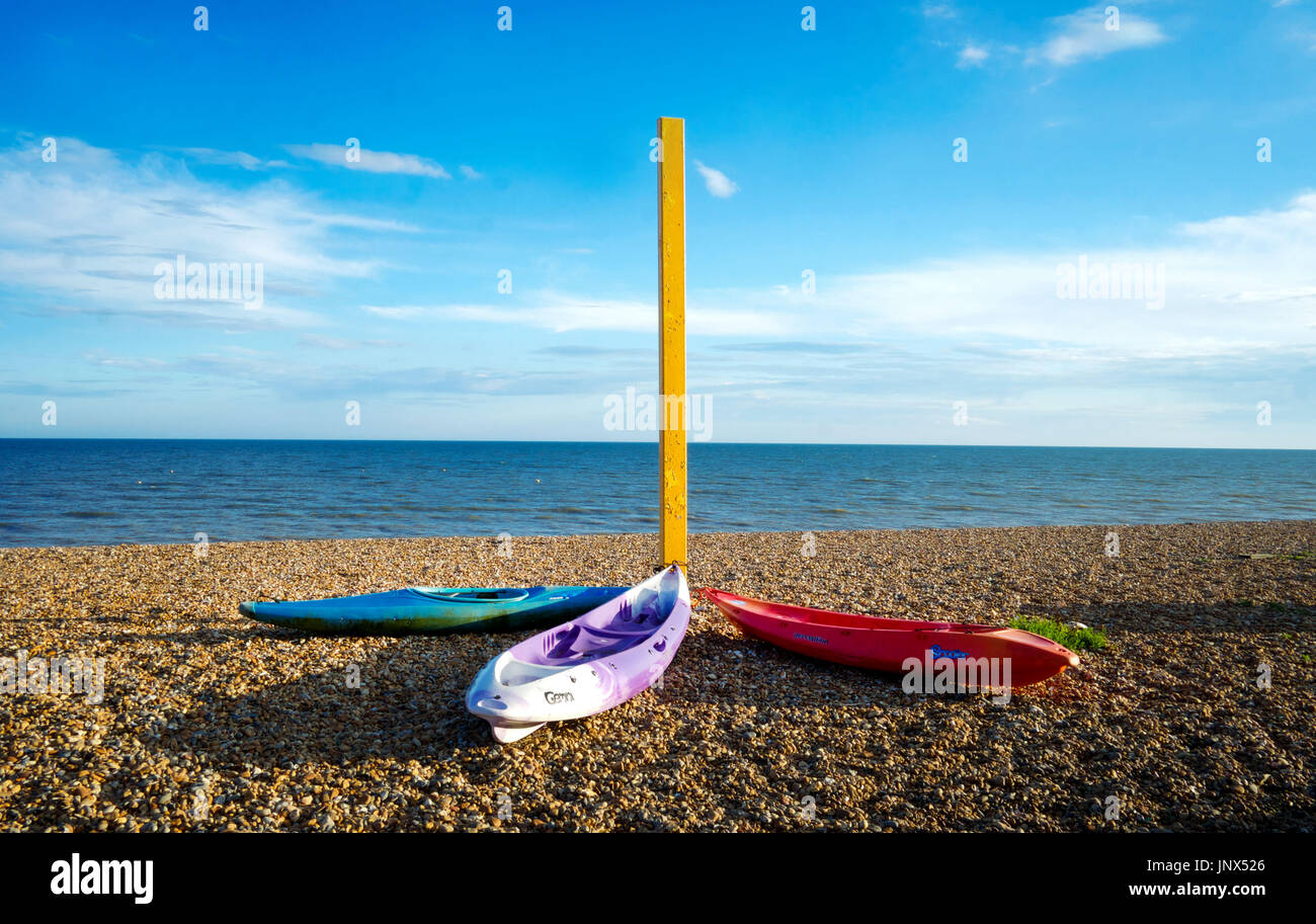 3 plastic canoes on a pebble beach tied to a metal yellow post on the