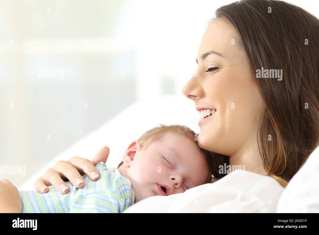 Side view portrait of a happy mother sleeping with her baby on a bed Stock Photo