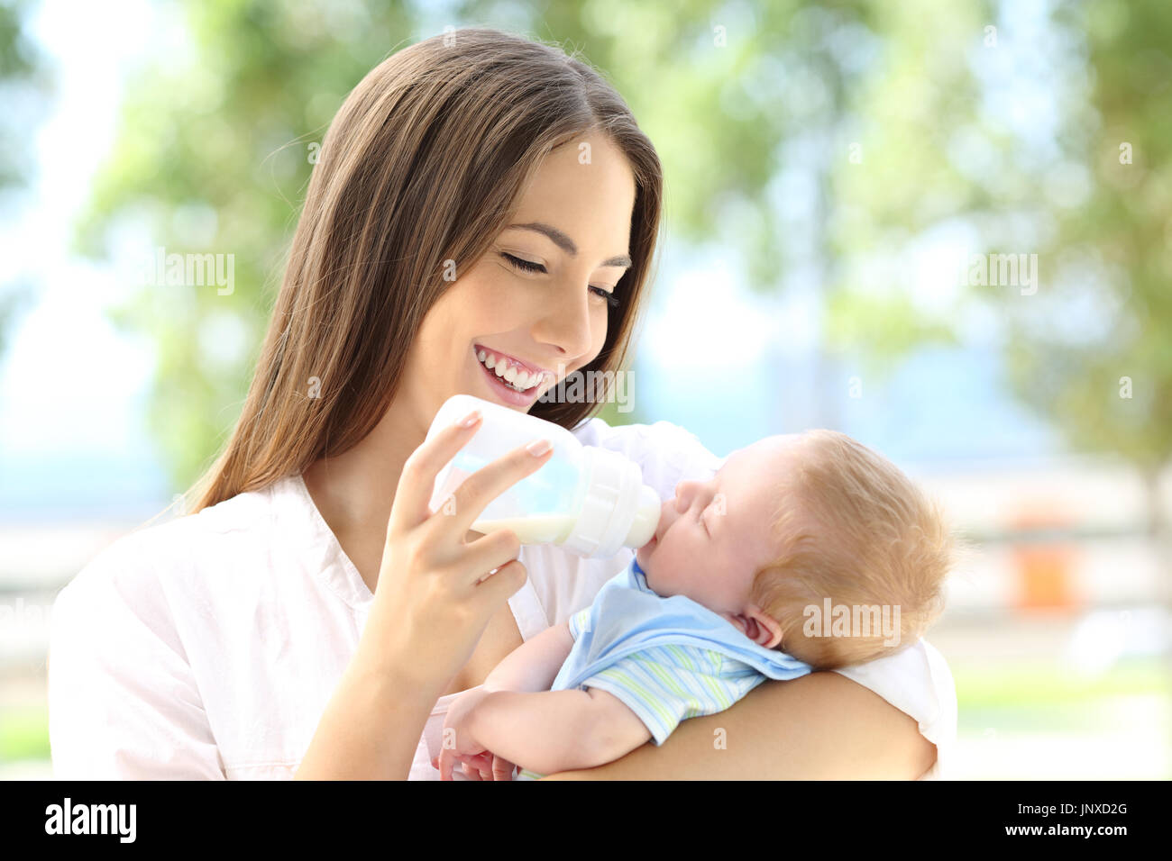 Portrait of a happy mother giving bottle feeding to her baby outdoors Stock Photo