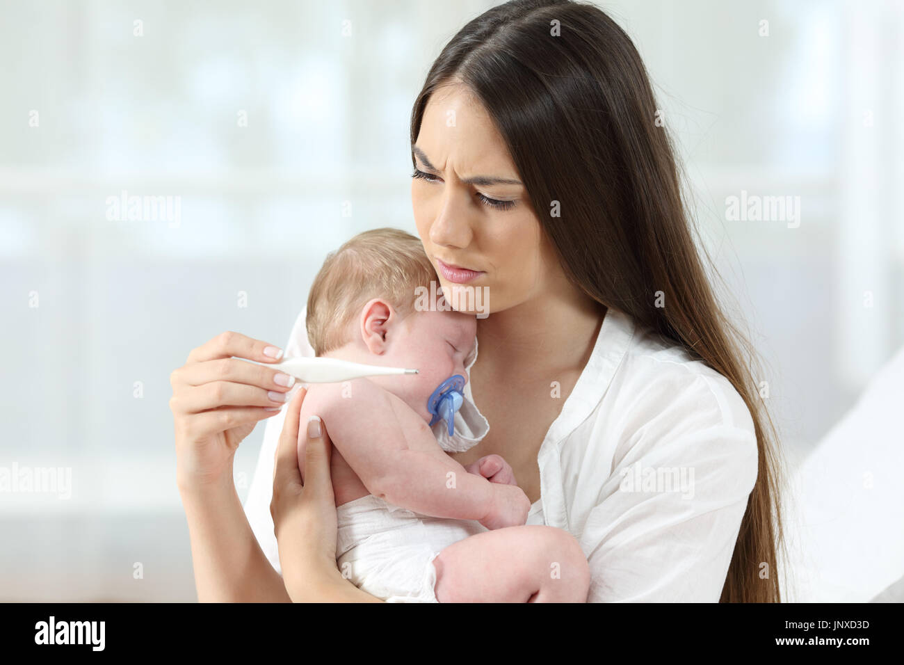 Mother checking thermometer holding her ill baby at home Stock Photo