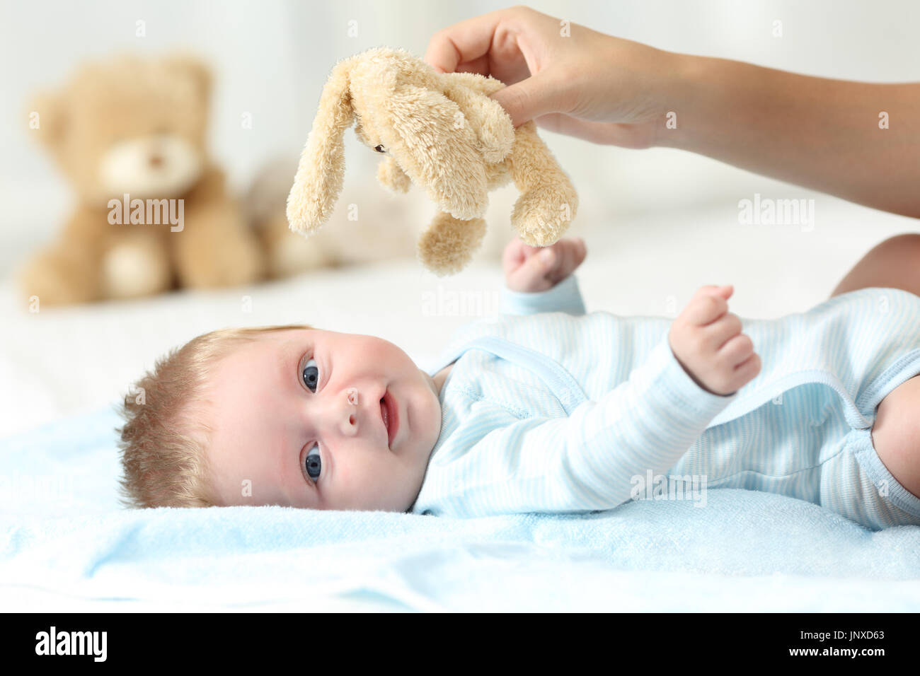 Mother hand holding a teddy and her baby looking at you on a bed Stock Photo