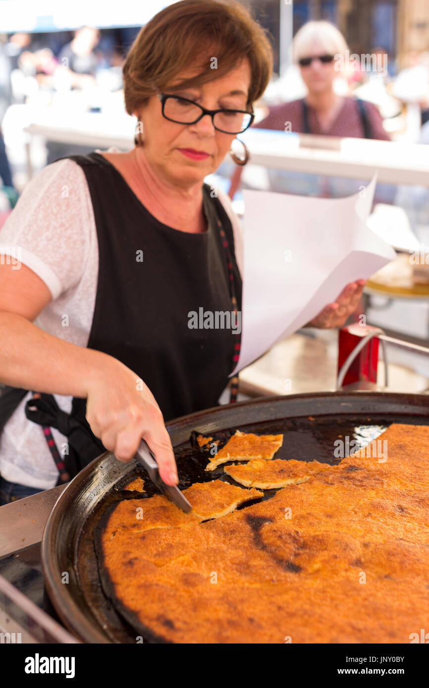 Nice, Alpes-Maritime Department, France - October 10, 2015: Woman in market in Nice, making and selling socca, a local delicacy. Stock Photo