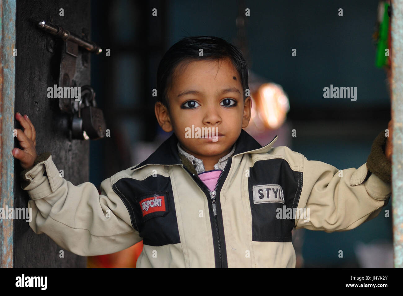 A child wearing traditional kajal eye protection stands in a doorway in Varanasi Stock Photo