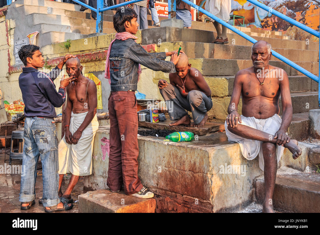 A man and a boy have their heads shaved by barbers on the ghats at Varanasi Stock Photo