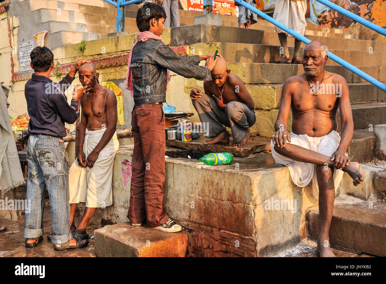 A man and a boy have their heads shaved by barbers on the ghats at Varanasi Stock Photo