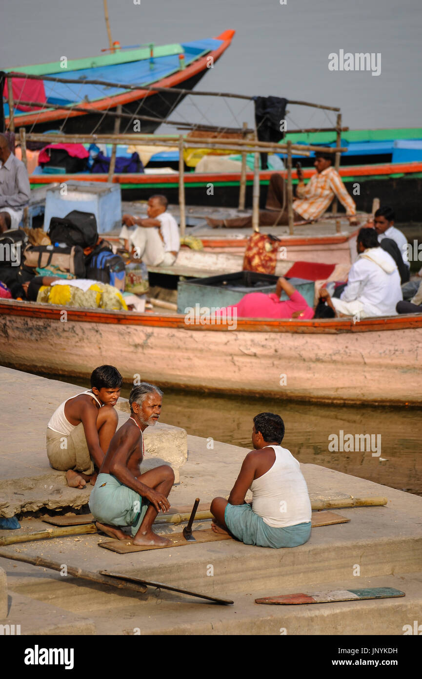 Men sit and talk by the Ganges as they make oars for their boats Stock Photo
