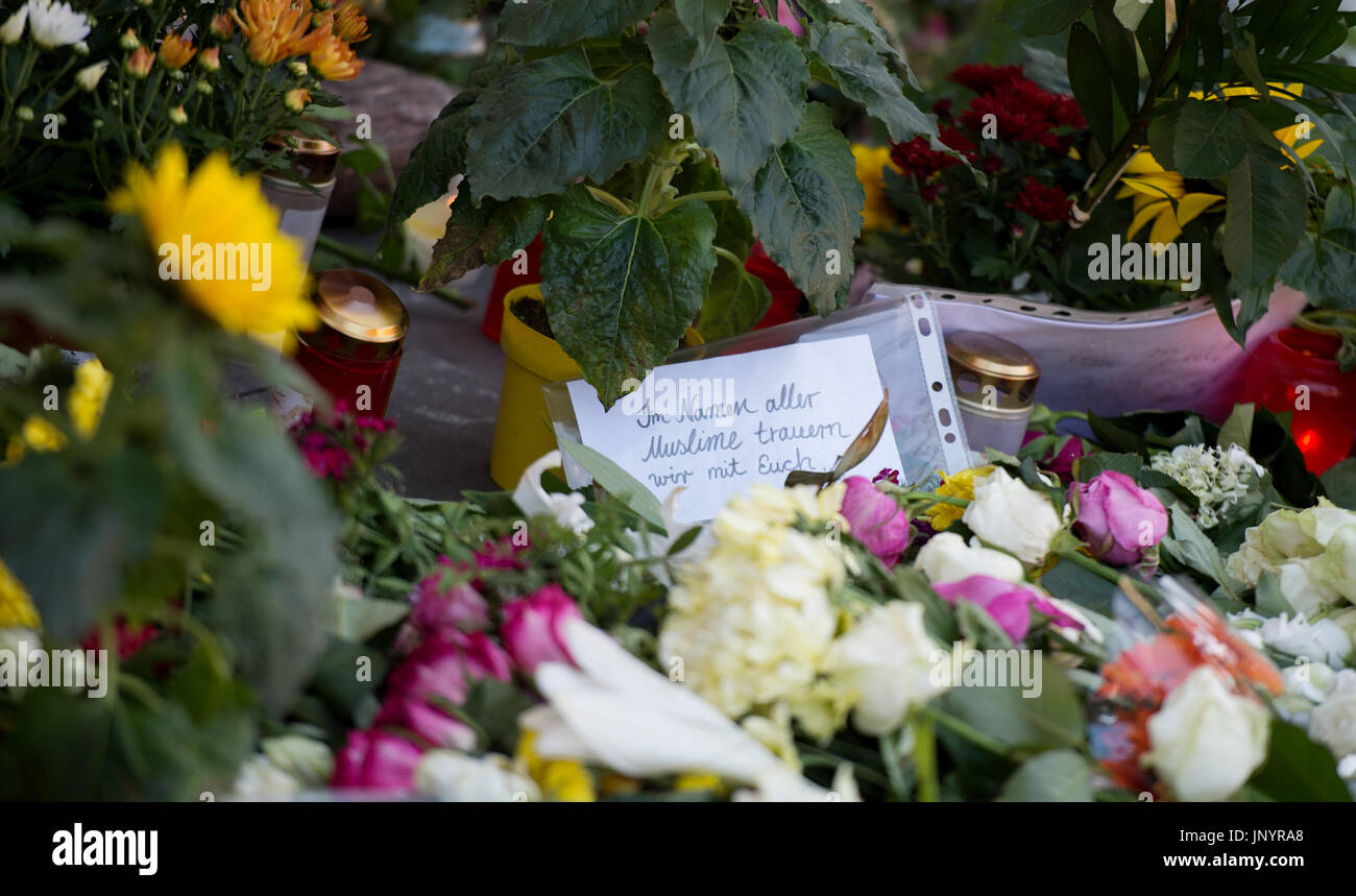 Several flowers and candles lie in front of a supermarket in Hamburg-Barmbek, Germany, 31 July 2017. During a knife attack a 26-year-old rejected asylum seeker killed a 50-year old man in the supermarket. Seven further people were seriously wounded. On a paper 'Im Namen aller Muslime trauern wir mit Euch' (lit. in the name if all muslums we mourn with you) can be read. Photo: Daniel Reinhardt/dpa Stock Photo
