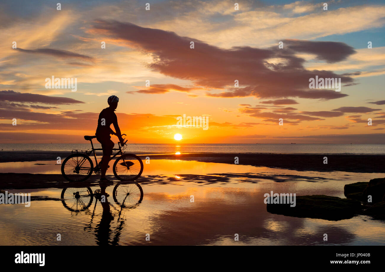 Mountain biker silhouetted on beach at sunrise. UK Stock Photo