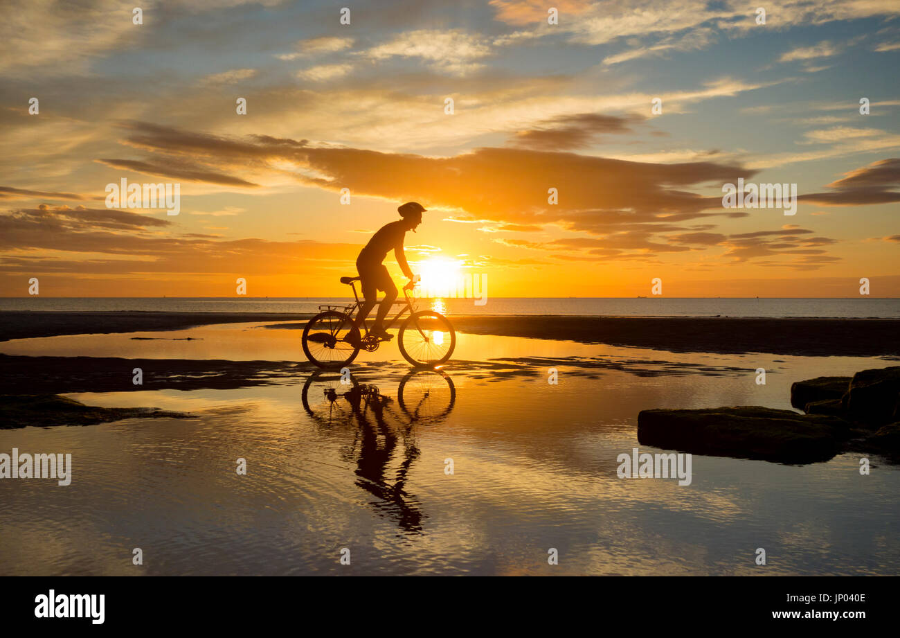 Mountain biker silhouetted on beach at sunrise. UK Stock Photo