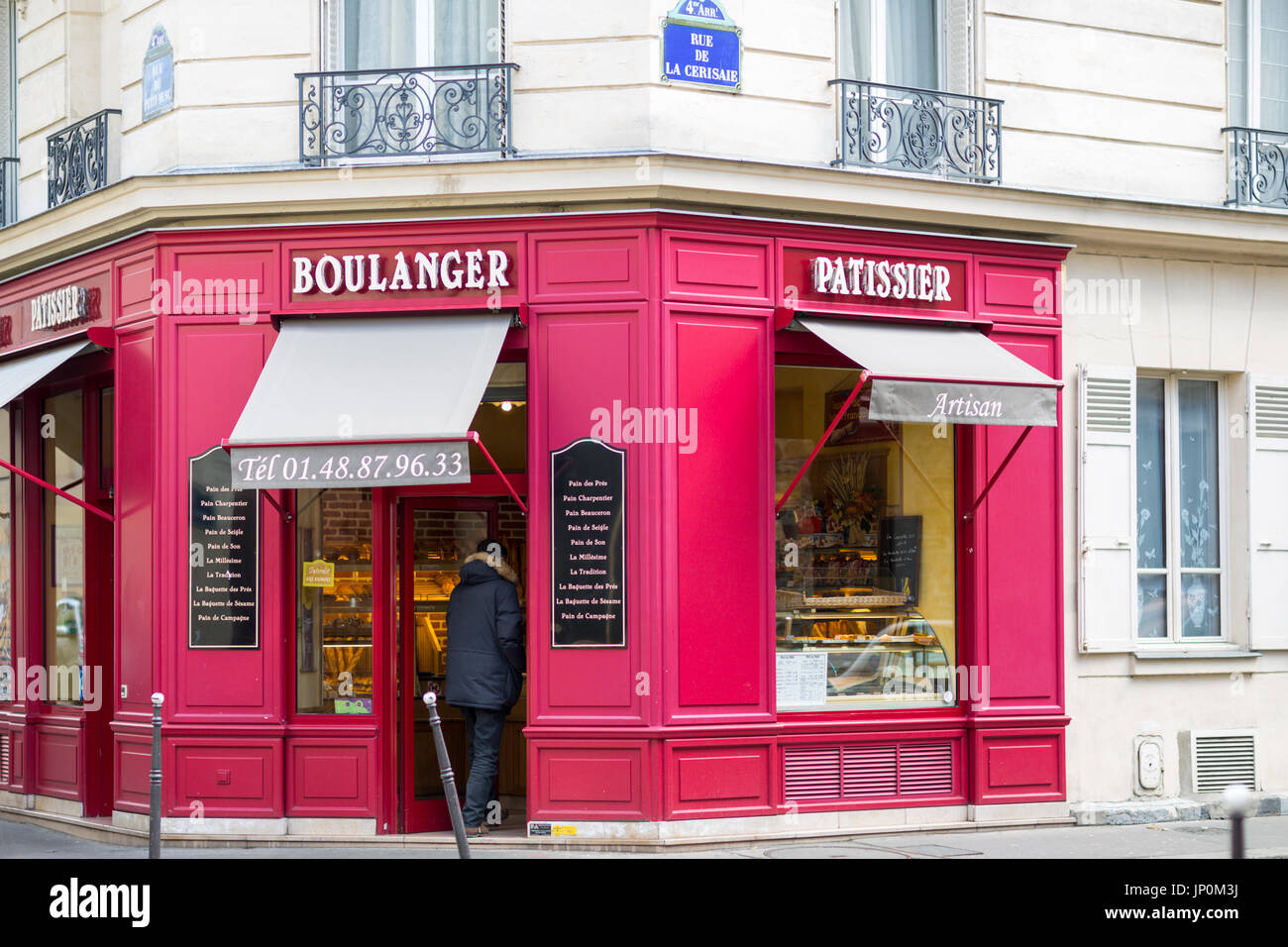Paris, France - March 2, 2016: Man entering red bakery and pastry shop on the corner of rue du Petit Musc and rue de la Cerisaie in the Marais, Paris. Stock Photo