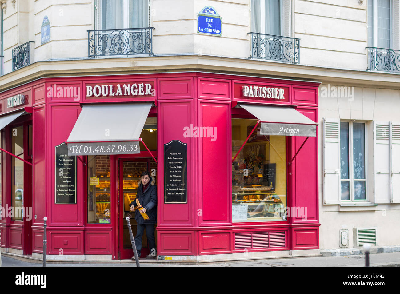 Paris, France - March 2, 2016: Man leaving red bakery and pastry shop on the corner of rue du Petit Musc and rue de la Cerisaie in the Marais, Paris, baguette in hand Stock Photo