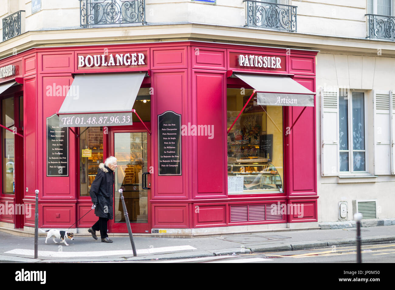 Paris, France - March 2, 2016: Woman walks her dog past red bakery and pastry shop on the corner of rue du Petit Musc and rue de la Cerisaie in the Marais, Paris. Stock Photo