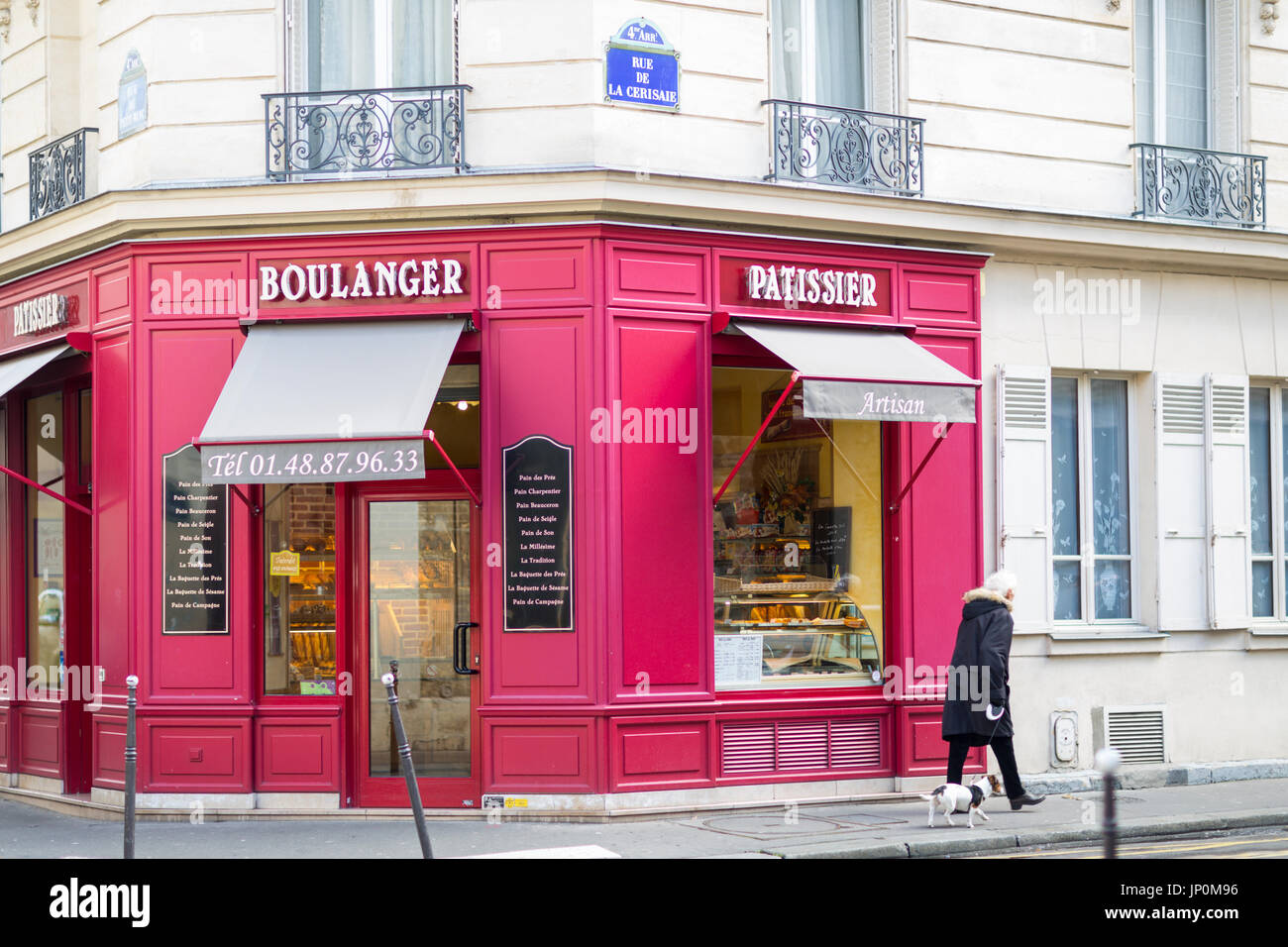 Paris, France - March 2, 2016: Woman walks her dog past red bakery and pastry shop on the corner of rue du Petit Musc and rue de la Cerisaie in the Marais, Paris. Stock Photo