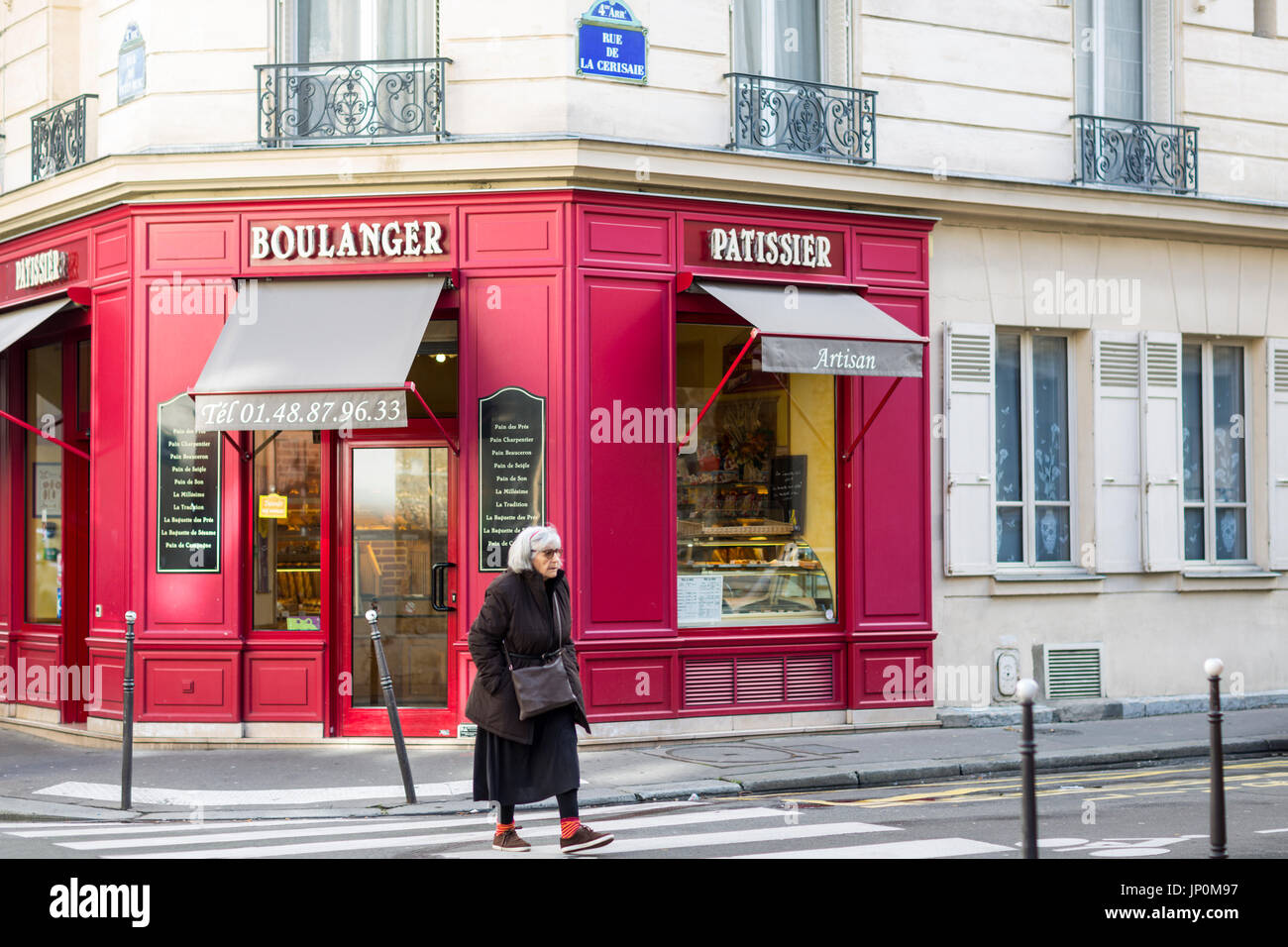 Paris, France - March 2, 2016: Woman crossing street by red bakery and pastry shop on the corner of rue du Petit Musc and rue de la Cerisaie in the Marais, Paris. Stock Photo