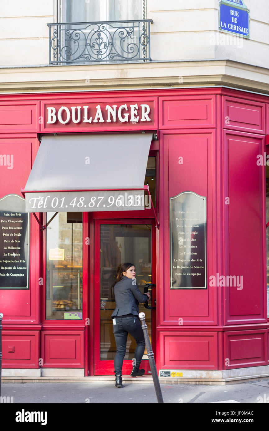 Paris, France - March 2, 2016: Young woman entering red bakery and pastry shop on the corner of rue du Petit Musc and rue de la Cerisaie in the Marais, Paris. Stock Photo