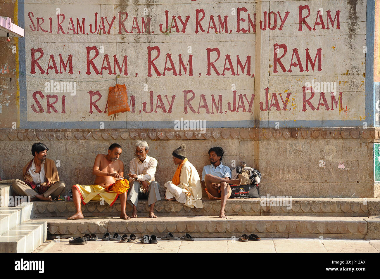Men relax and share paan under a large mural of a chant to Lord Rama Stock Photo