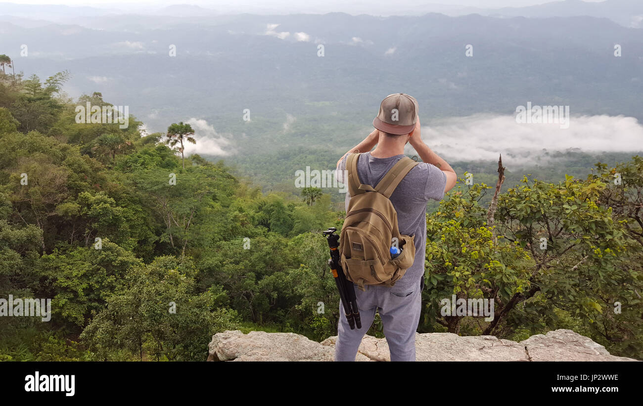 man solo traveler photographer taking pictures of a foggy valley from the edge of a cliff in the jungle on the mountain. Stock Photo