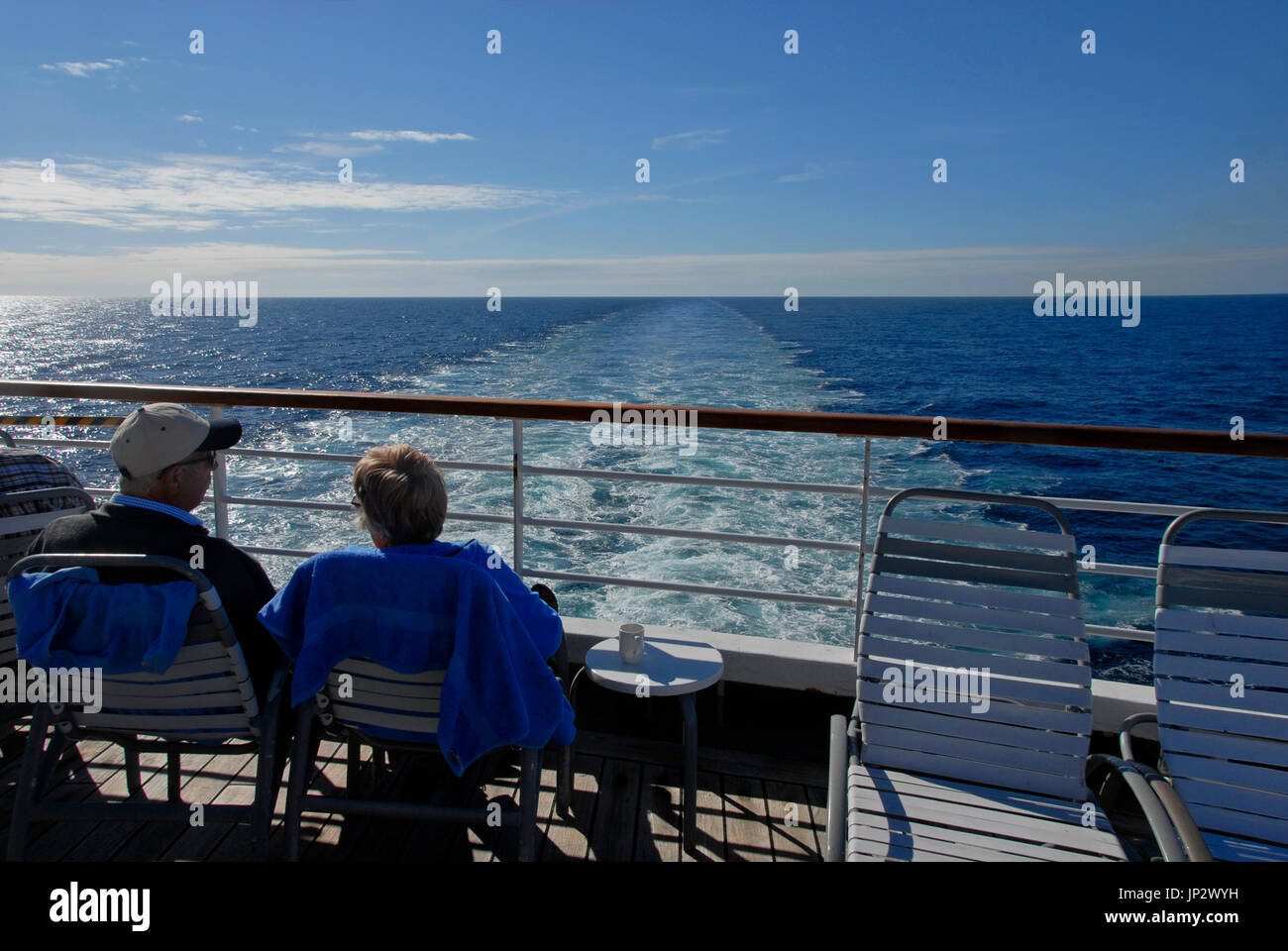 Couple sitting on stern of cruise liner watching the wake Stock Photo