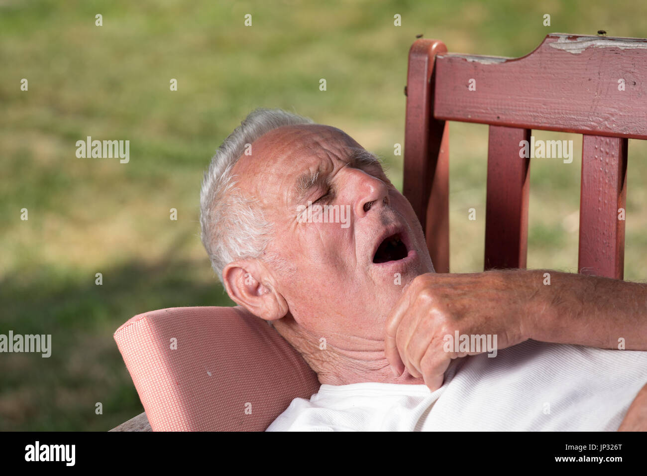 Senior man lying on bench in garden and feeling sleepy. Yawning and preparing for siesta Stock Photo