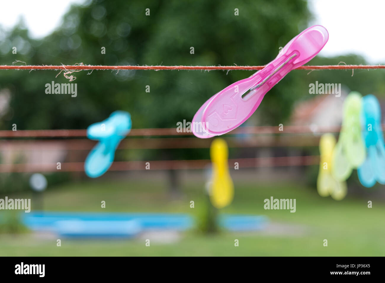 clothespins clipped on a strings, garden with pool in background Stock Photo