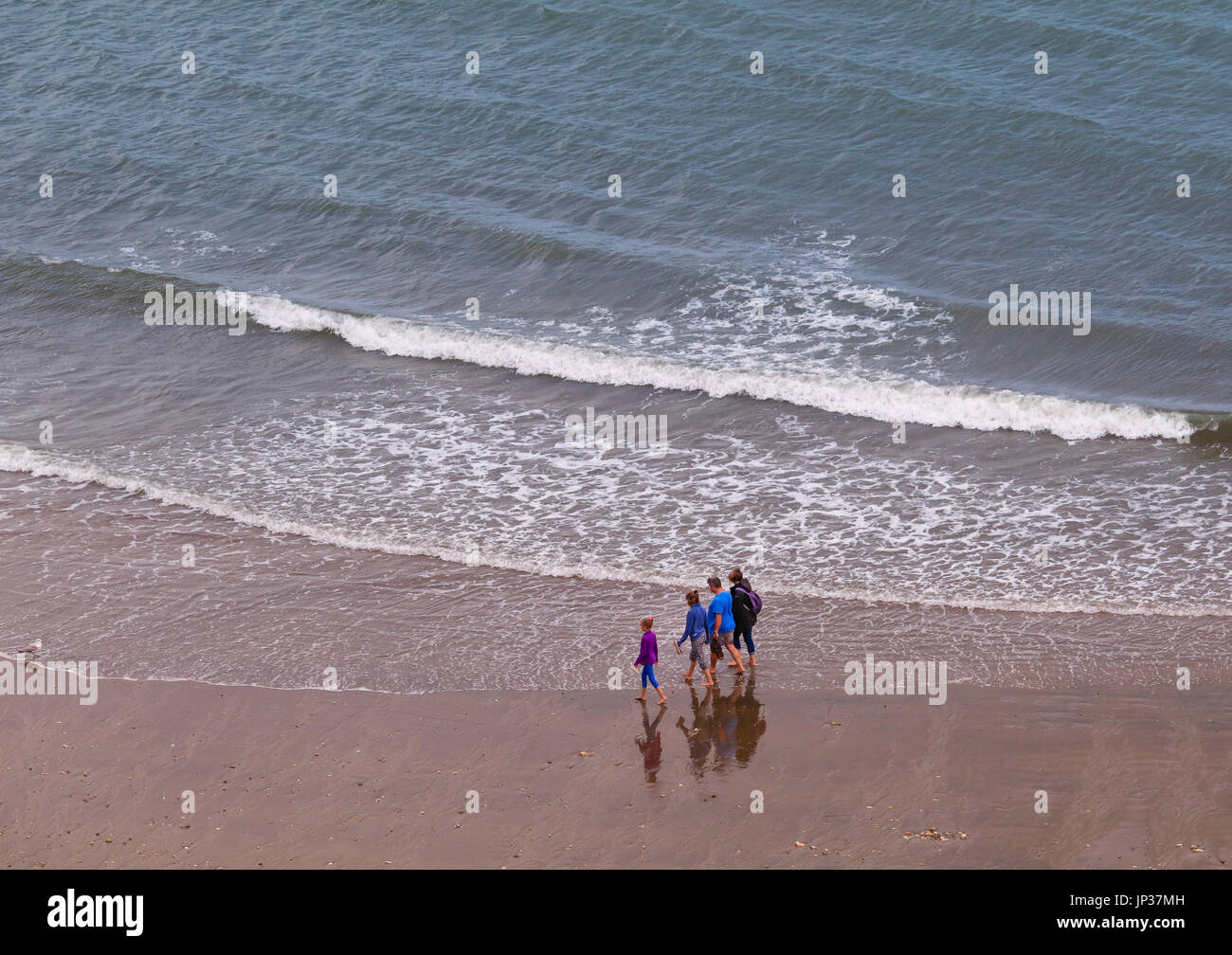 Family walking by the shore; waves in the background; reflections of people on wet sand Stock Photo