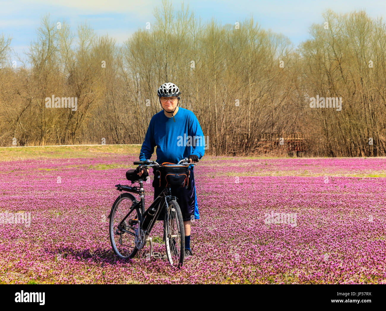 Senior man bicyclist standing in the middle of a field covered with henbit wildflowers smiling; Missouri, Midwest; spring Stock Photo