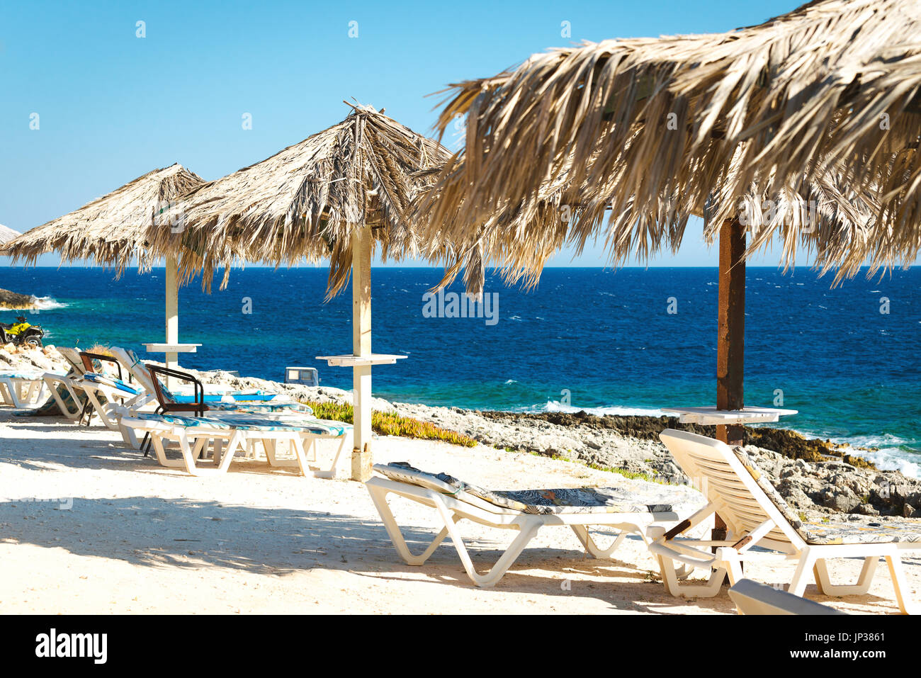 Romantic place near the sea. Summertime vacation holidays background. Sunny beach with sunbeds under umbrellas Stock Photo