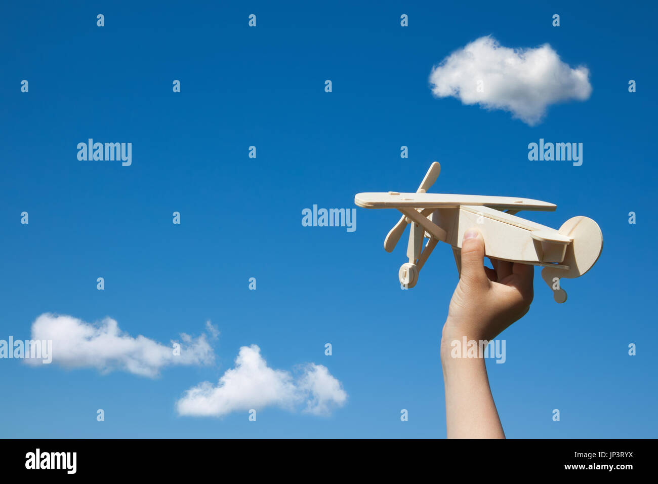 Wooden plane in child hand on the blue sky and clouds background. ( With space for text.) Stock Photo