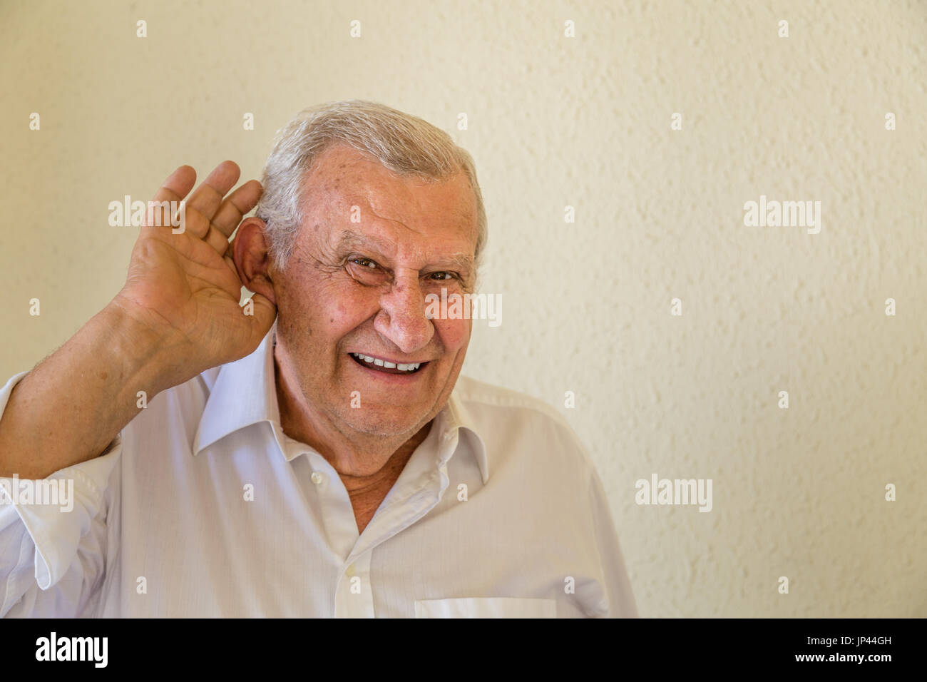 Cheerful man puts a hand to the ear to hear better isolated over yellow wall background, old man is listening to something Stock Photo