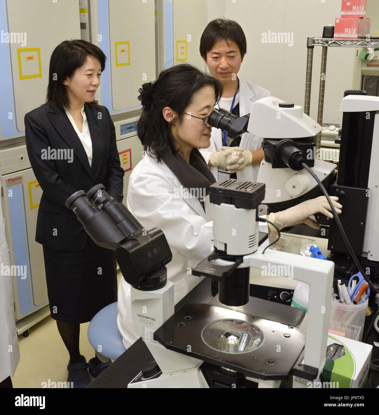 OSAKA, Japan - Masayo Takahashi (L), project leader at Riken Center for Developmental Biology, inspects an experiment at Riken's stem cell culture laboratory in Kobe, western Japan, in February 2013. A Japanese team has recently conducted the world's first surgery to implant tissue derived from induced pluripotent stem cells into a human body as part of the clinical study led by Takahashi and others. (Kyodo) Stock Photo