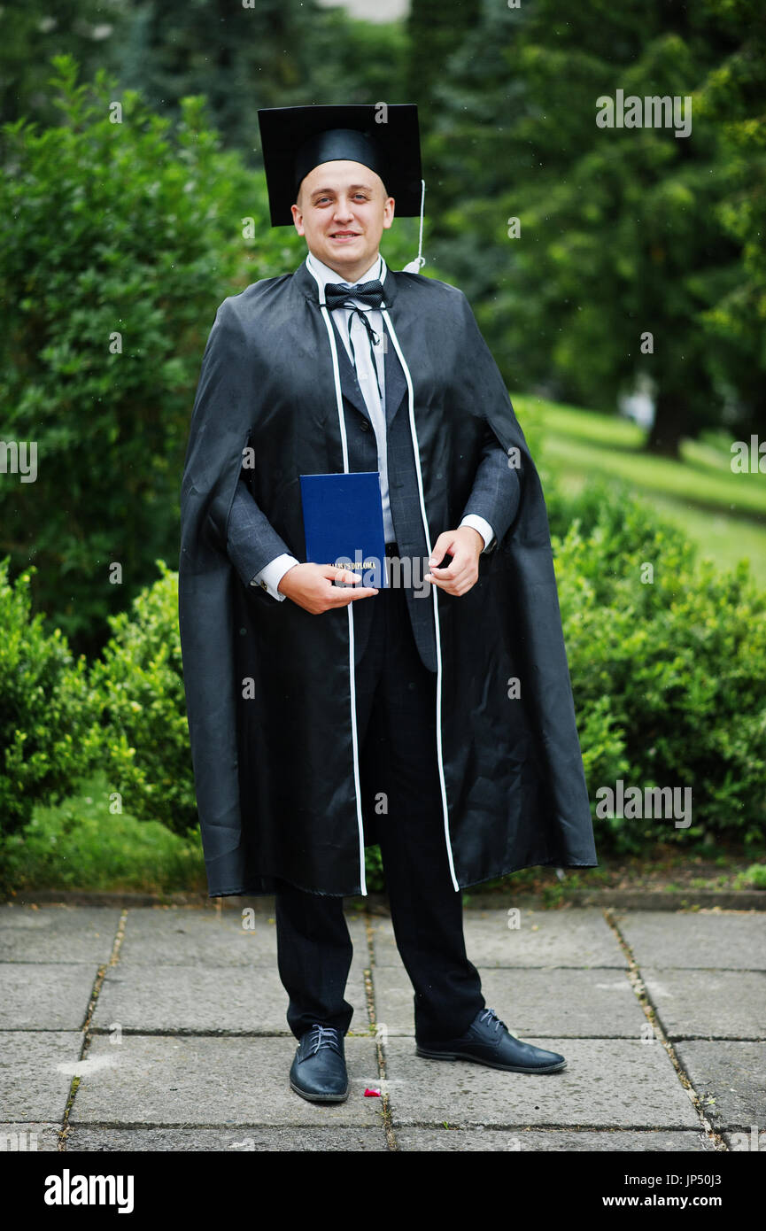Portrait of an elegant young man in park dressed in graduation gown and ...