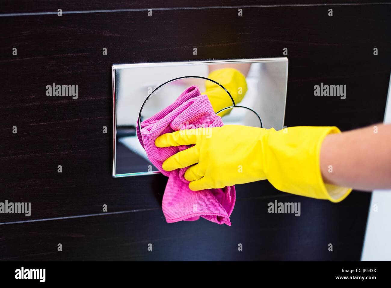 Female hands with yellow rubber protective gloves cleaning toilet flush button with pink cloth. Spring cleaning Stock Photo