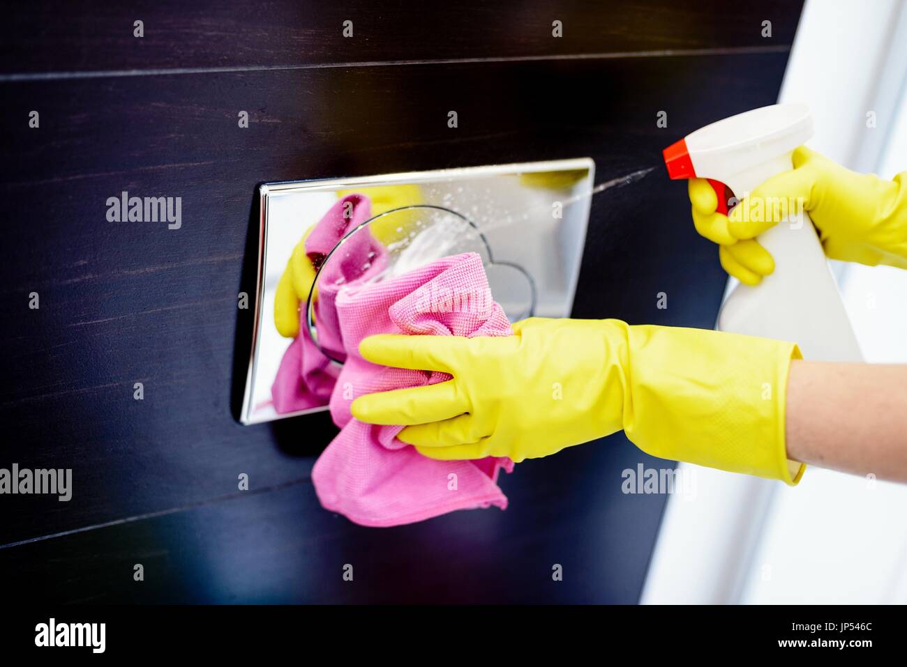 Female hands with yellow rubber protective gloves cleaning toilet flush button with pink cloth and spray detergent. Spring cleaning Stock Photo