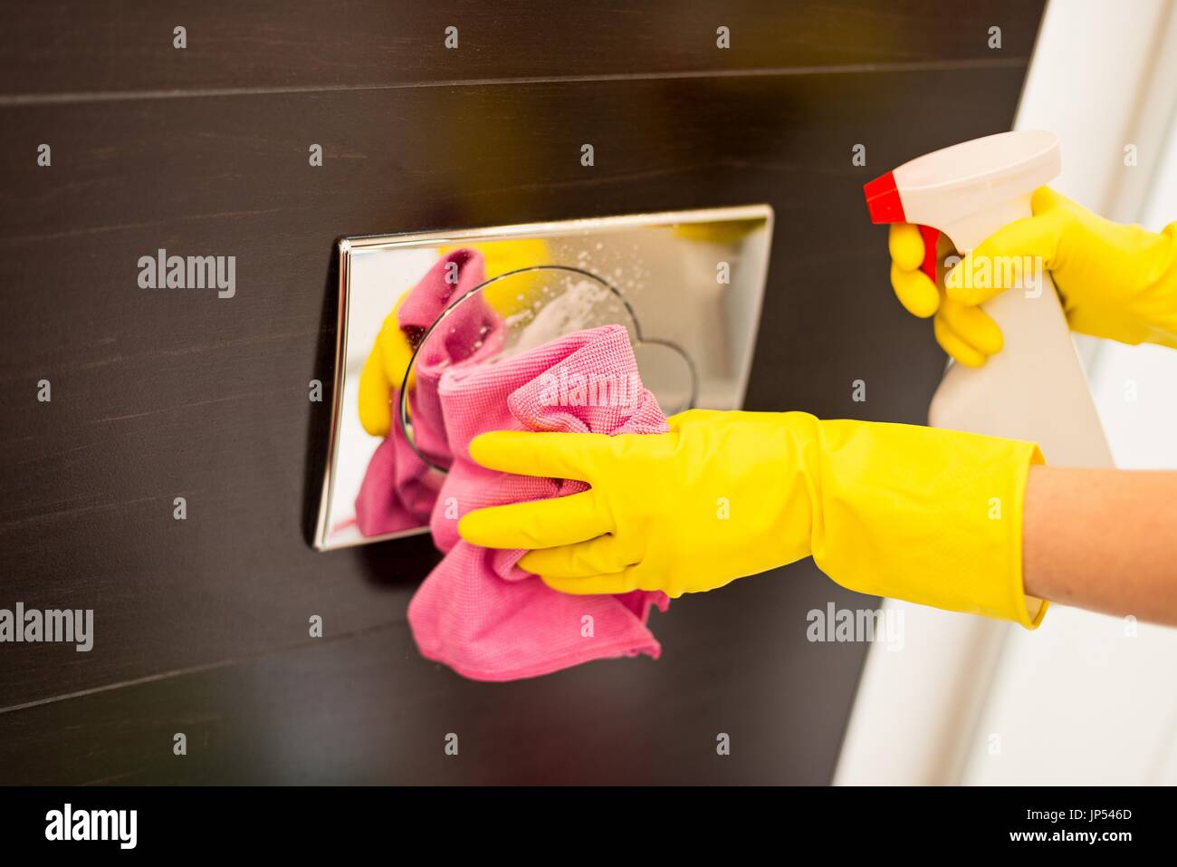 Female hands with yellow rubber protective gloves cleaning flush button in toilet. Spring cleaning Stock Photo