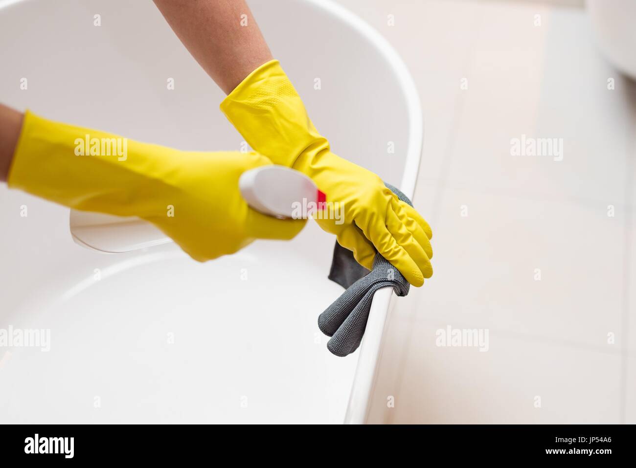 Hands with yellow rubber gloves holding detergent spray bottle and ...