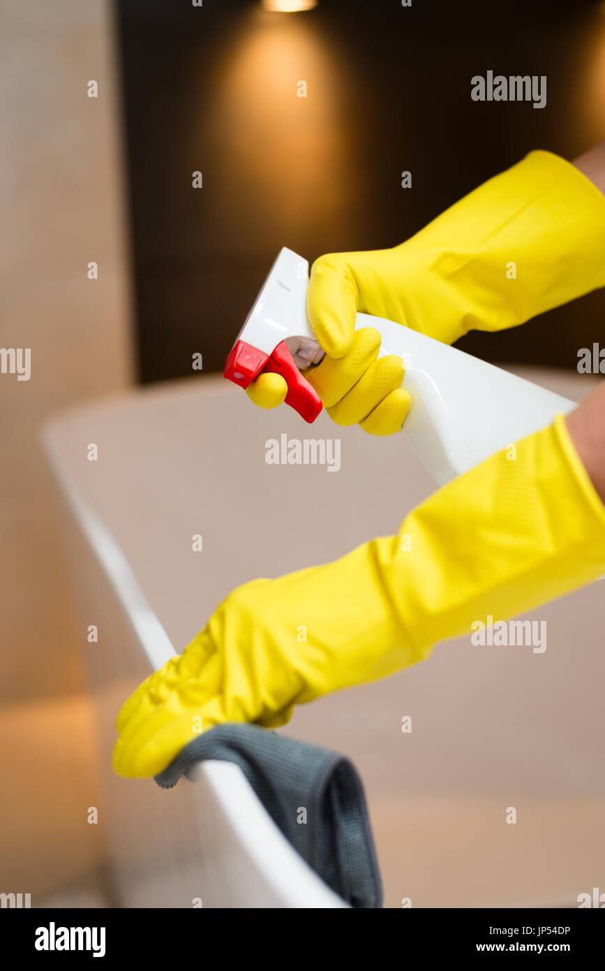 Hands with yellow rubber gloves holding detergent spray bottle and ...