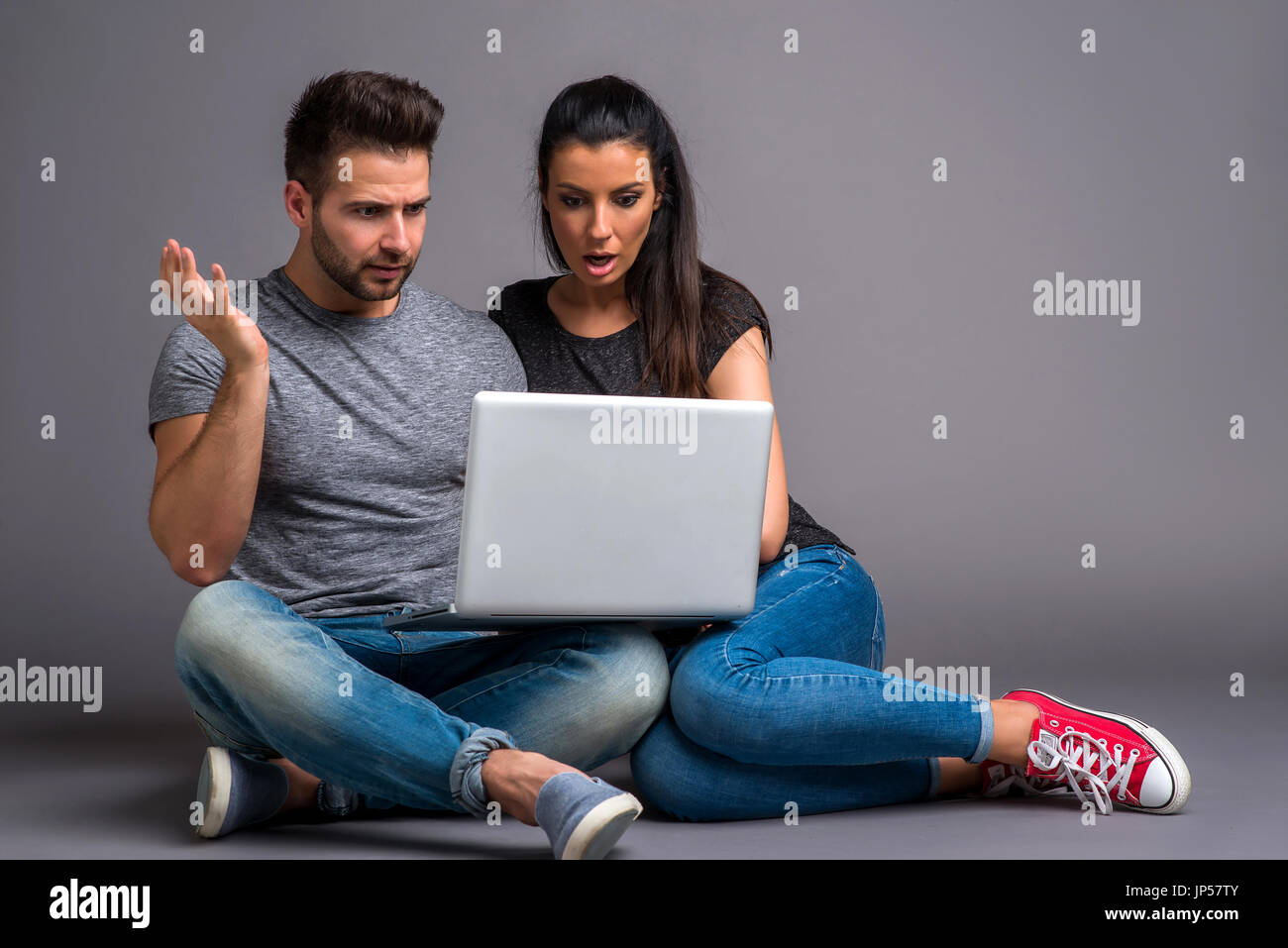 A beautiful young couple sitting on the ground and looking at a laptop and feeling surprised Stock Photo