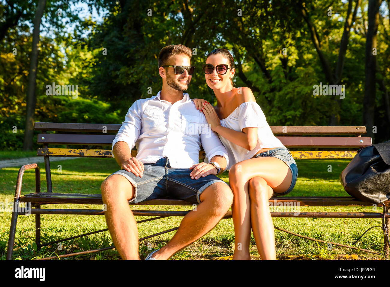 A beautiful young couple sitting on a bench in a park in the sunset ...