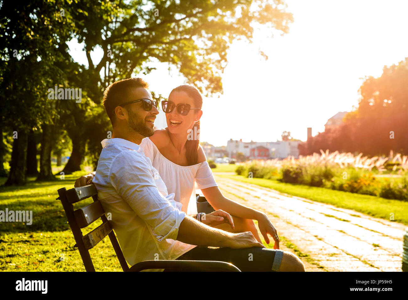 A beautiful young couple sitting on a bench in a park in the sunset ...