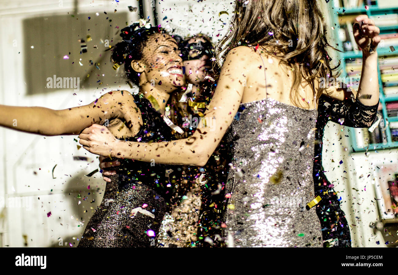 Four women wearing cocktail dresses dancing in a shower of confetti. Stock Photo