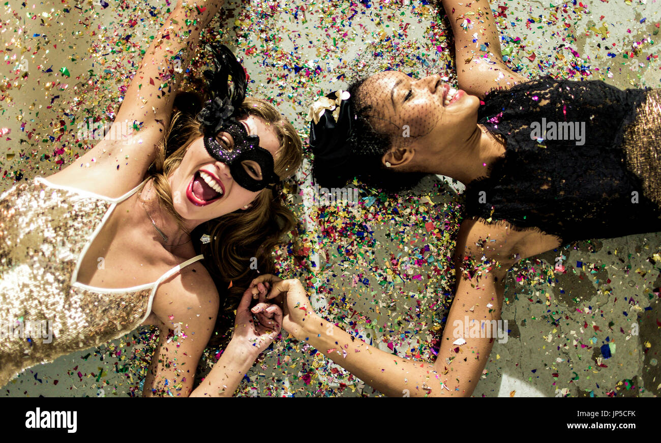 Two women wearing cocktail dresses at a party lying on the floor in a shower of confetti. Stock Photo