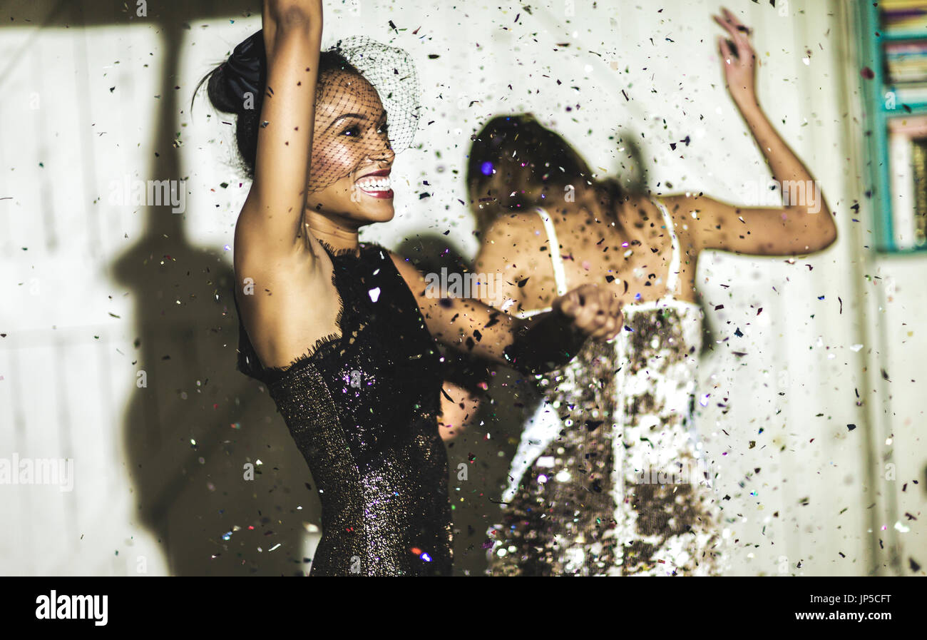 Two women wearing cocktail dresses at a party dancing in a shower of glitter confetti. Stock Photo