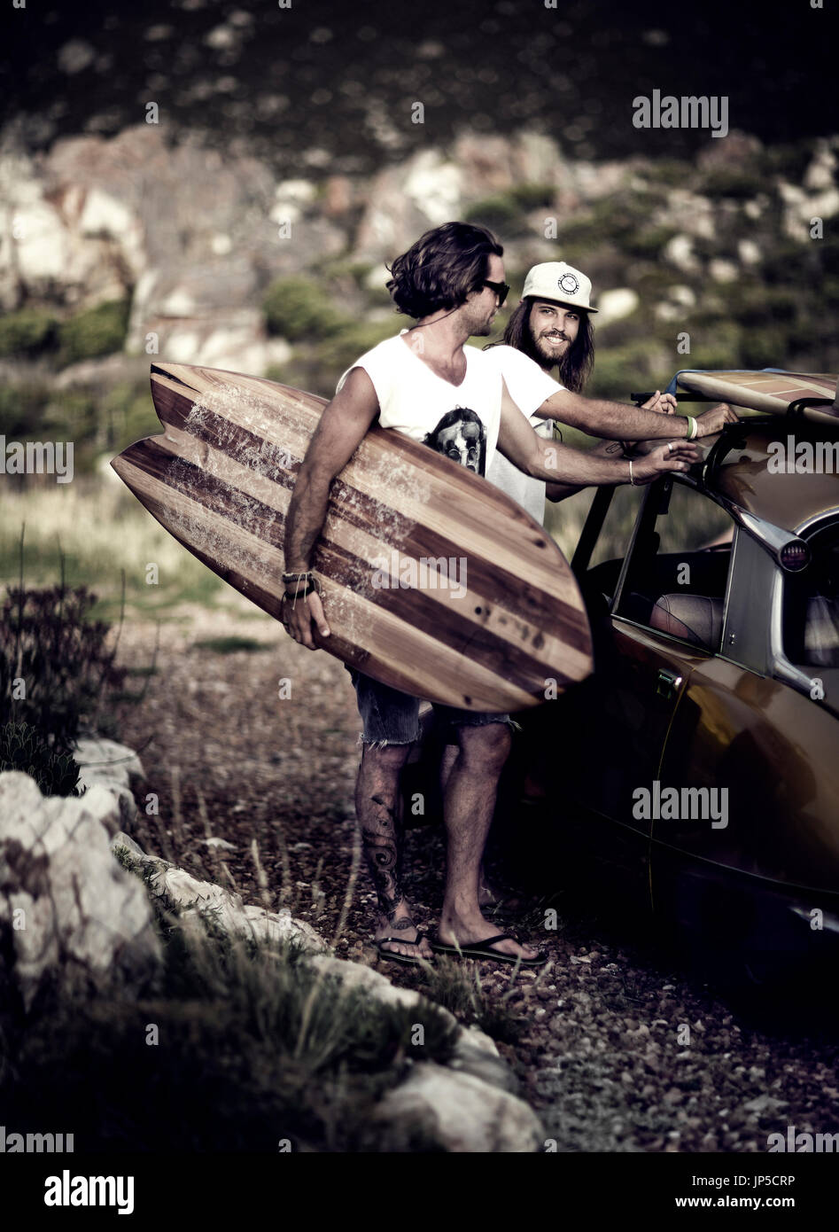 Two young men standing next to car, carrying surfboard. Stock Photo