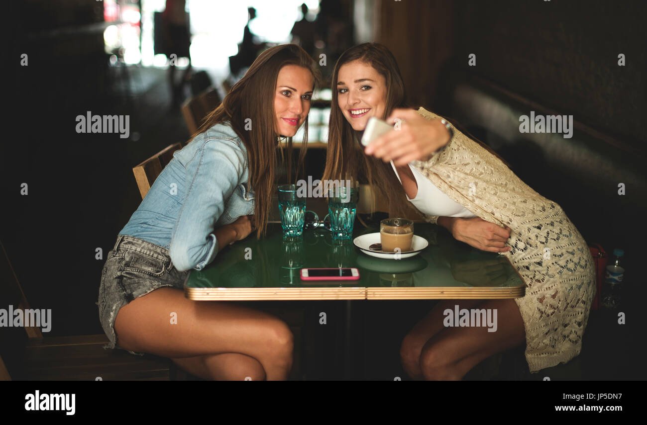 Two young women sitting at a cafe table posing for a selfie. Stock Photo